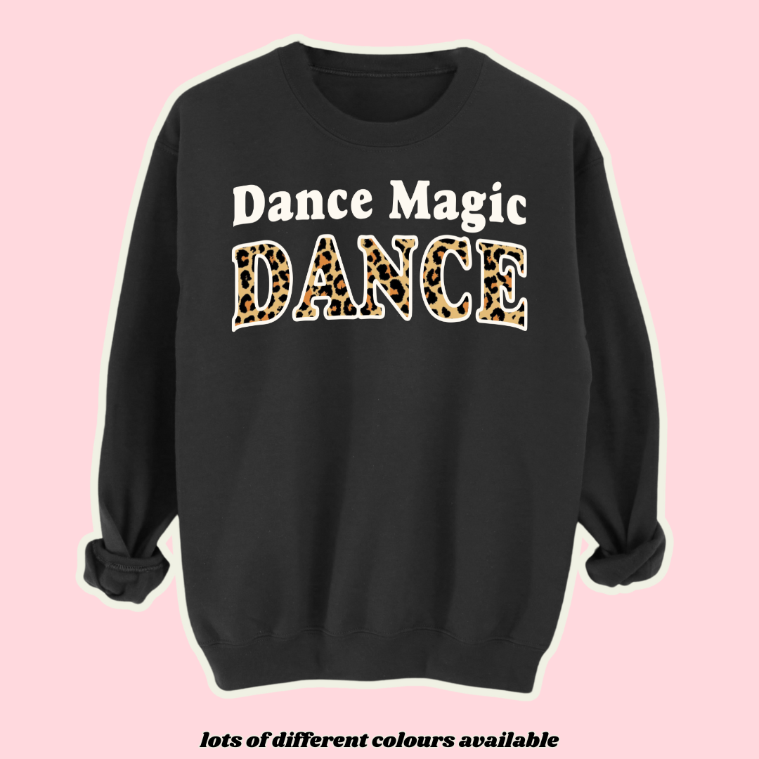 Black fleece-lined sweatshirt with 'Dance Magic Dance' text inspired by the Labyrinth movie. Features bold white and leopard print lettering, embracing 90s fashion, retro music culture, and statement streetwear. Perfect for David Bowie fans and lovers of vintage-inspired style.